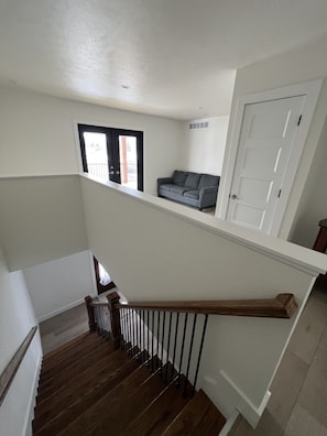 Eine Treppe mit Holzdielen und schwarzen Geländern führt zu einer Zwischenebene mit einem grauen Sofa und einer weißen Tür.
