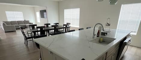 Una cocina moderna con una isla grande, luces colgantes y una zona de comedor con un sofá y sillas.