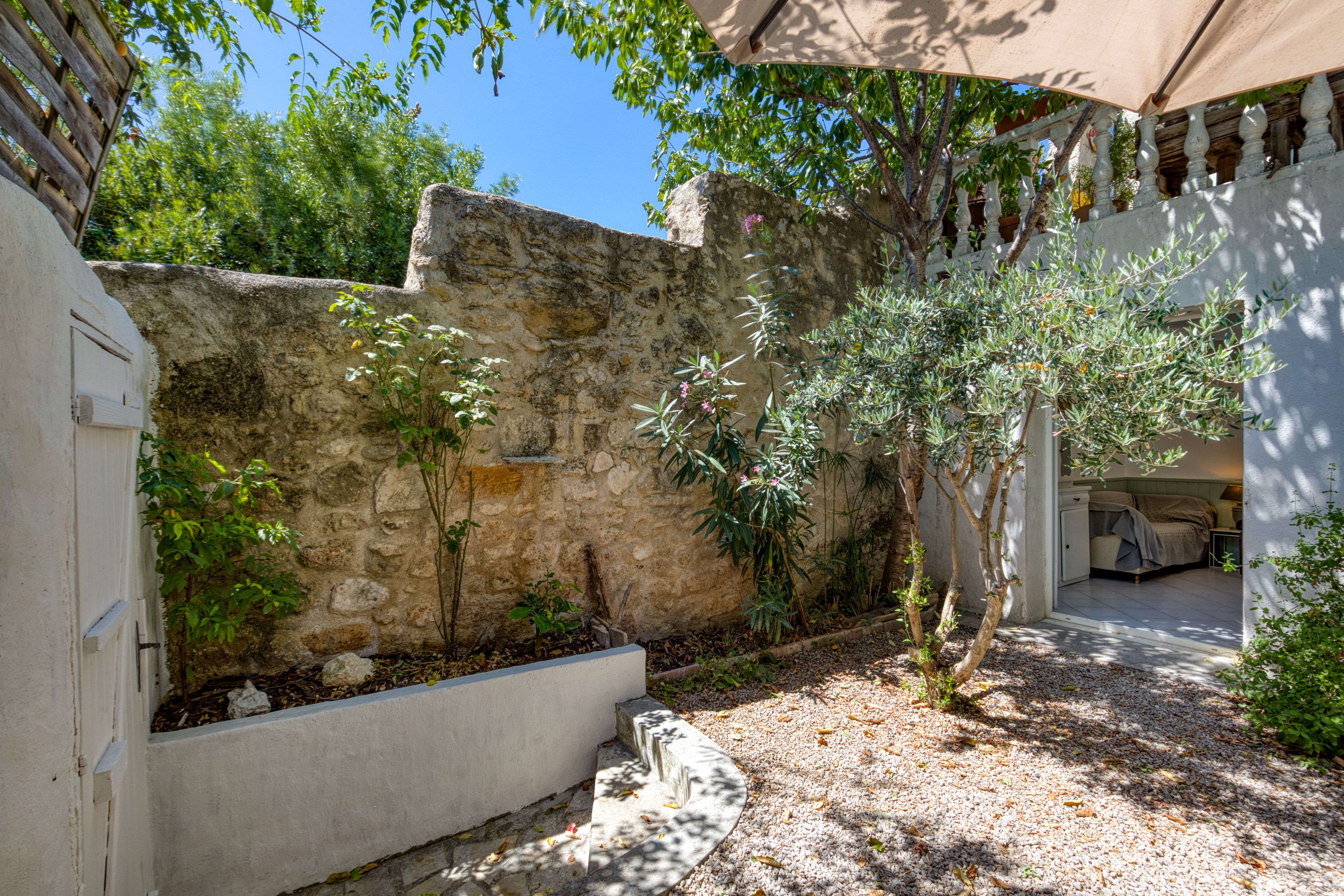 Ein Innenhof mit Steinmauer, einem kleinen Baum und einem Bett unter einer Pergola.