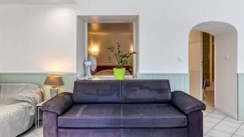 Un salon avec un canapé de couleur foncée, une petite table avec une lampe et une plante verte.