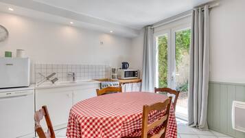 Een keuken met een eettafel, afgedekt met een geruit tafelkleed, houten stoelen, een witte koelkast, een magnetron en een gootsteen.