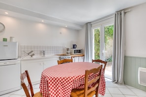 Een keuken met een eettafel, afgedekt met een geruit tafelkleed, houten stoelen, een witte koelkast, een magnetron en een gootsteen.