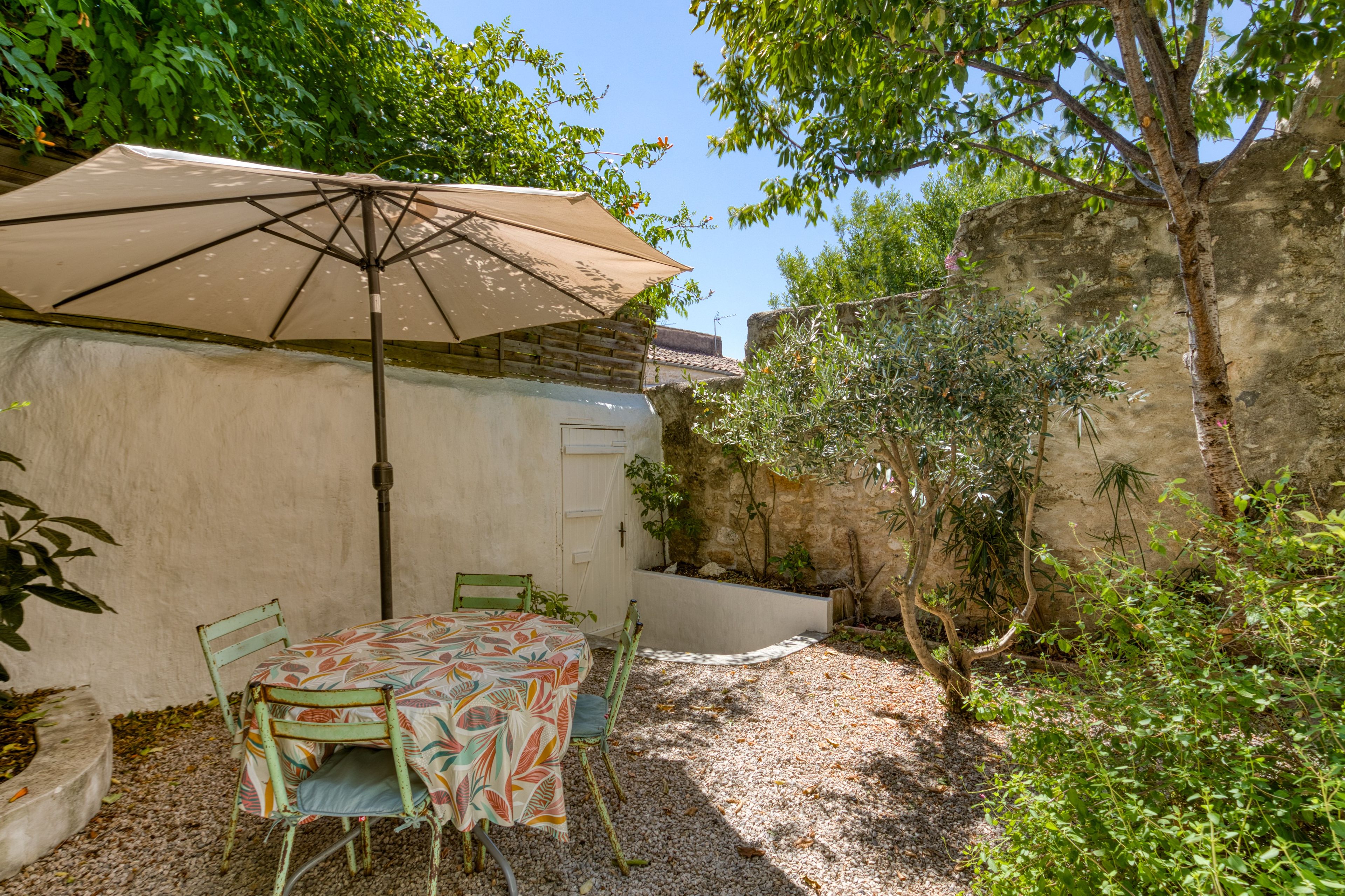 Een terras buiten met een tafel, stoelen, een grote parasol en een stenen muur.