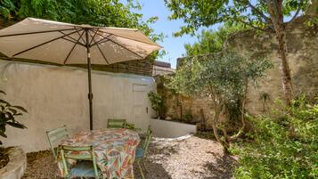 Een terras buiten met een tafel, stoelen, een grote parasol en een stenen muur.