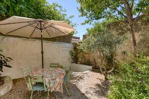 Een terras buiten met een tafel, stoelen, een grote parasol en een stenen muur.