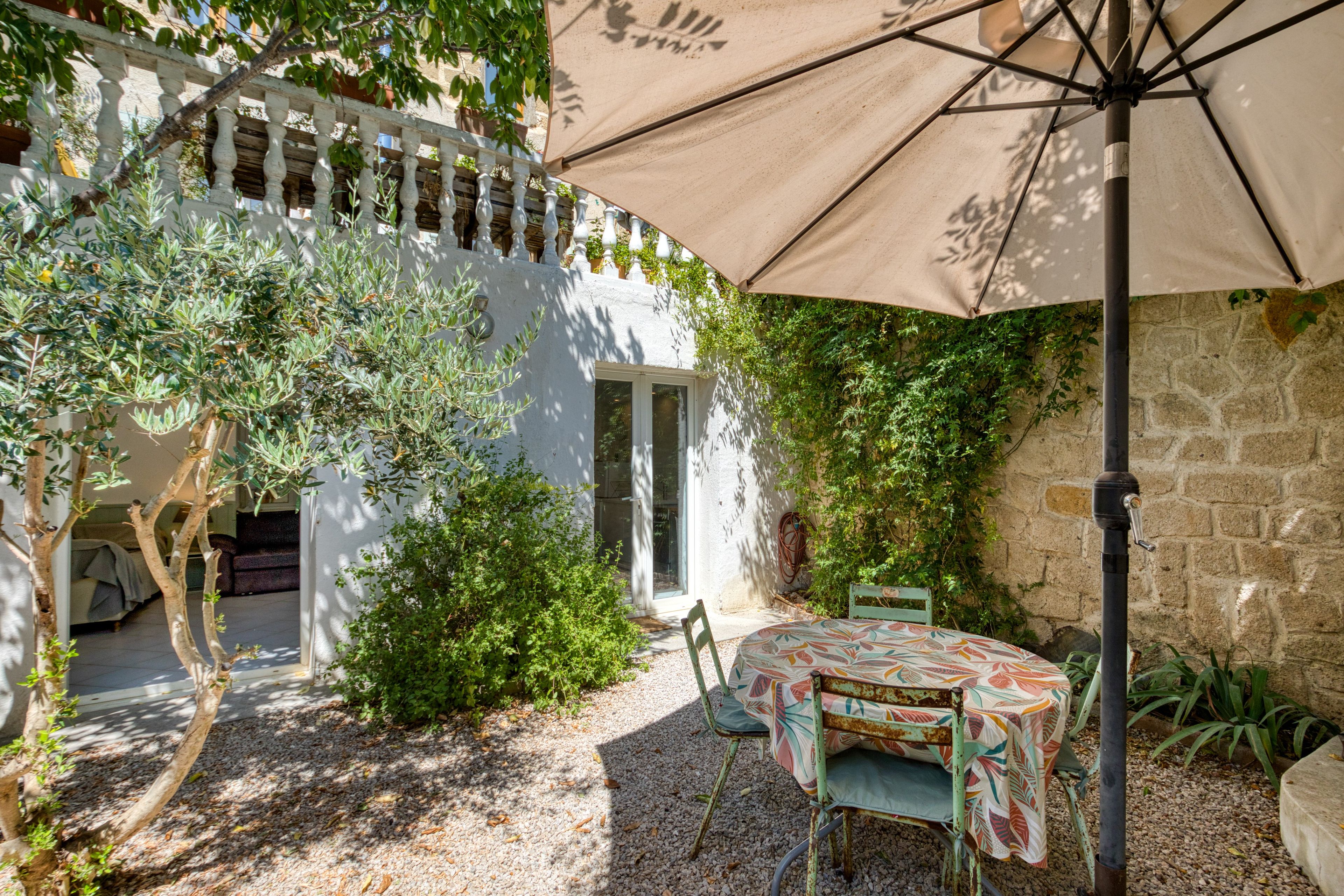 A patio with a table and chairs, a white fence, and greenery.
