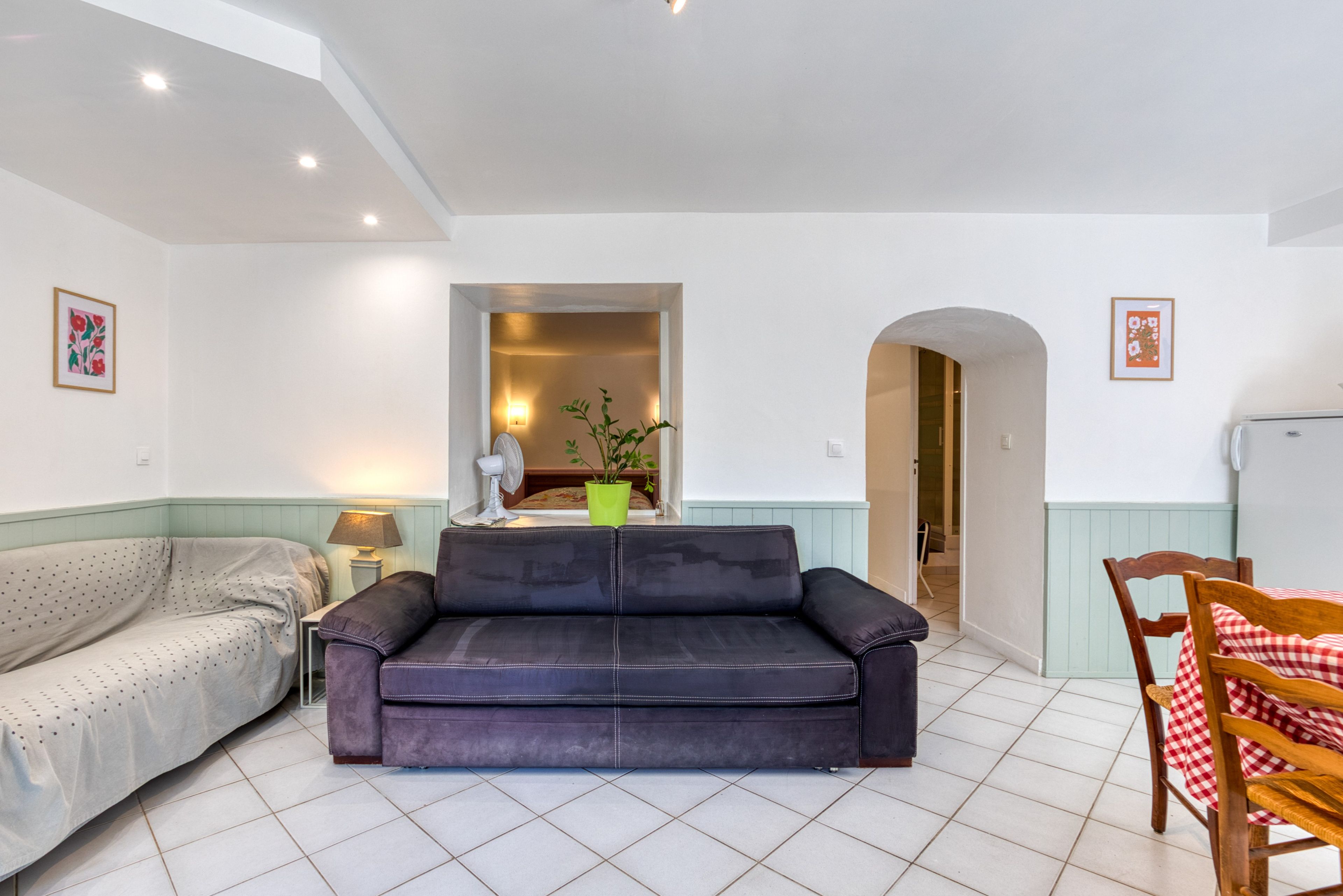 A living room with a sofa, a dining table with chairs, and a kitchen area in the background.