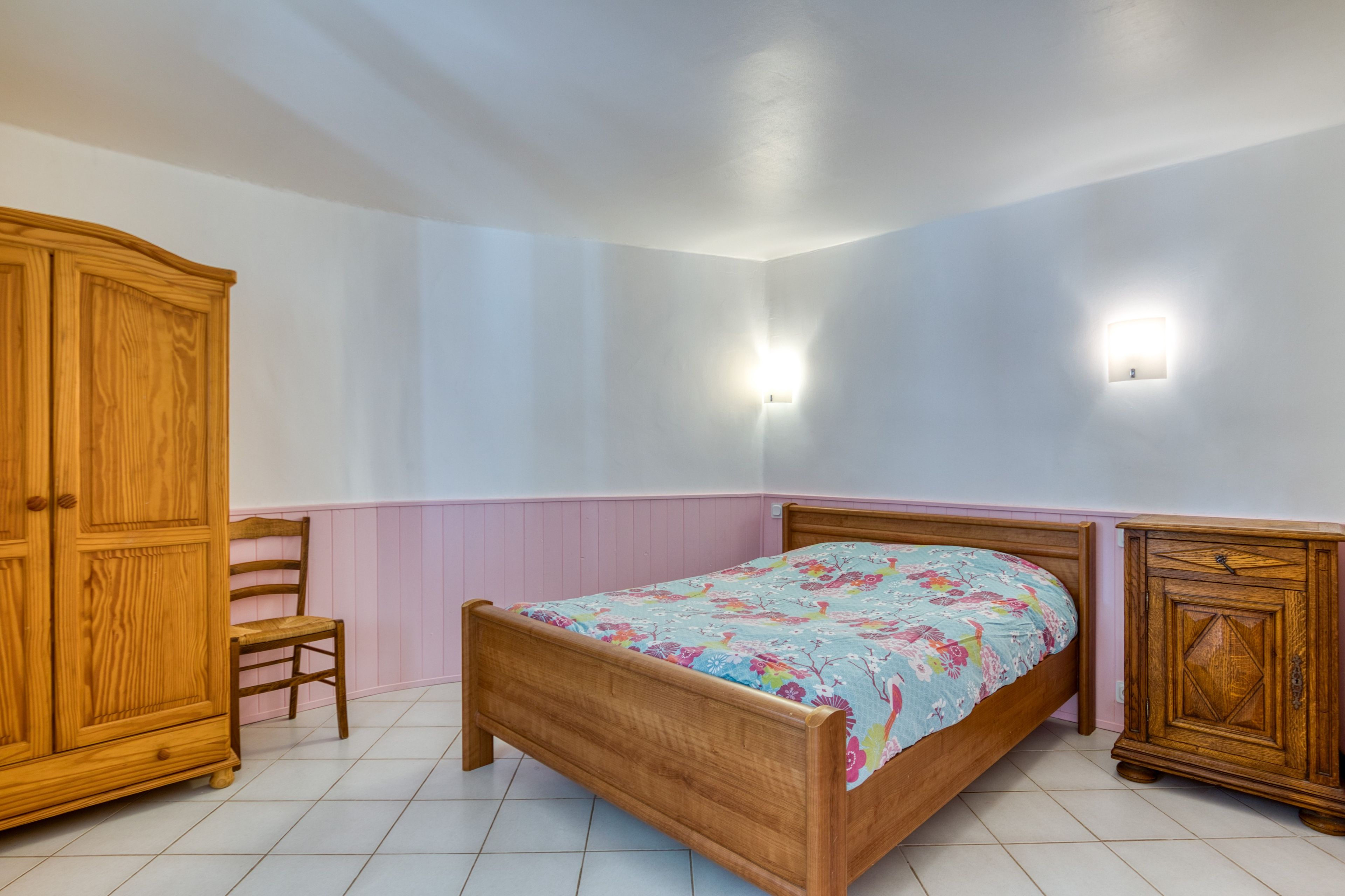Een slaapkamer met een houten bed, een houten kledingkast, een stoel en twee wandlampen.