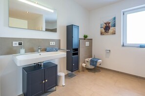 Une salle de bain moderne équipée d’un lavabo, d’un miroir, d’un meuble de rangement, de toilettes et d’une fenêtre.