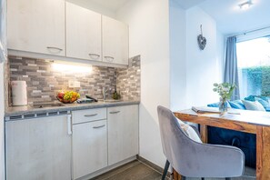 A modern kitchen with light-colored cabinets, a tiled backsplash, and a dining area with a wooden table and a chair. - Apartment Unternberg (Ruhpolding)