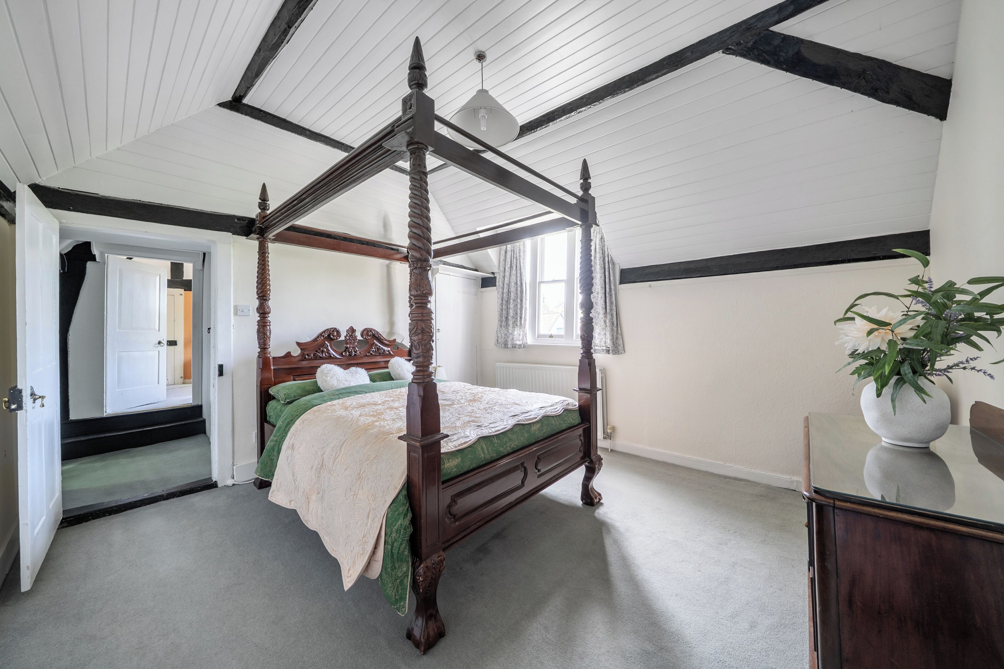A four-poster bed with a green bedspread, a wooden dresser, and a potted plant.
