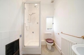 A bathroom with a glass-enclosed shower, a toilet, a window, and a radiator.