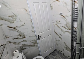Un baño con azulejos de mármol, un inodoro, un perchero para toallas y una puerta.