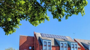Un immeuble à plusieurs étages, doté de panneaux solaires sur le toit, d’une façade en briques et d’une entrée sécurisée par un portail.