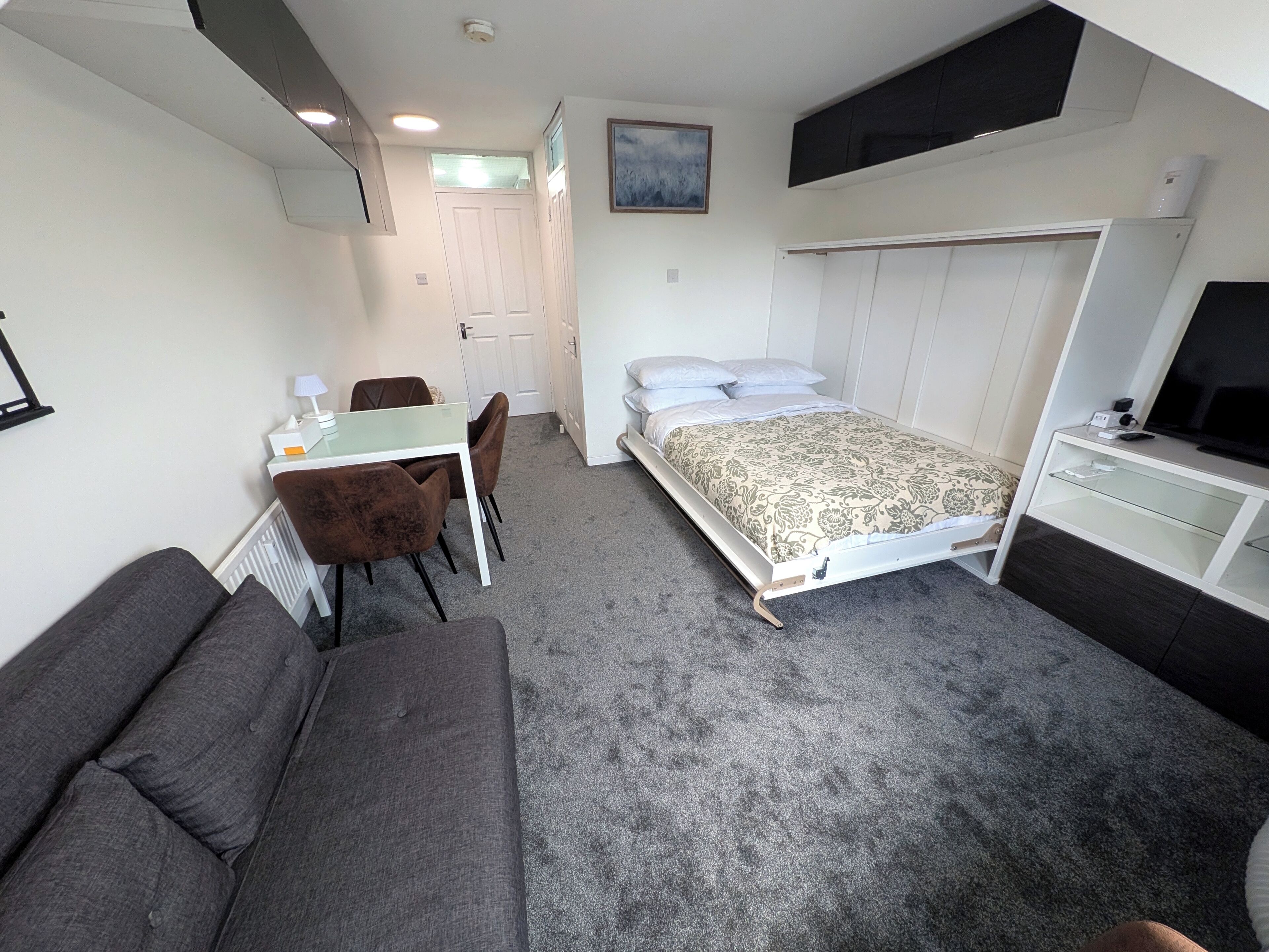 Ein kleines Zimmer mit einem Bett, einem Schreibtisch, einem Sessel, einer Couch und einem Fernseher.
