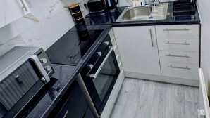 Une cuisine de taille réduite avec des meubles blancs, un plan de travail noir, une machine à café, un grille-pain et un évier.
