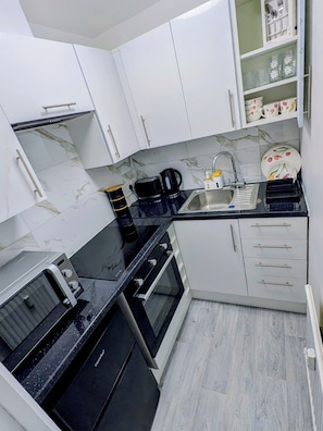 Una cocina compacta con armarios blancos, una encimera negra, cafetera, tostadora y un lavamanos.