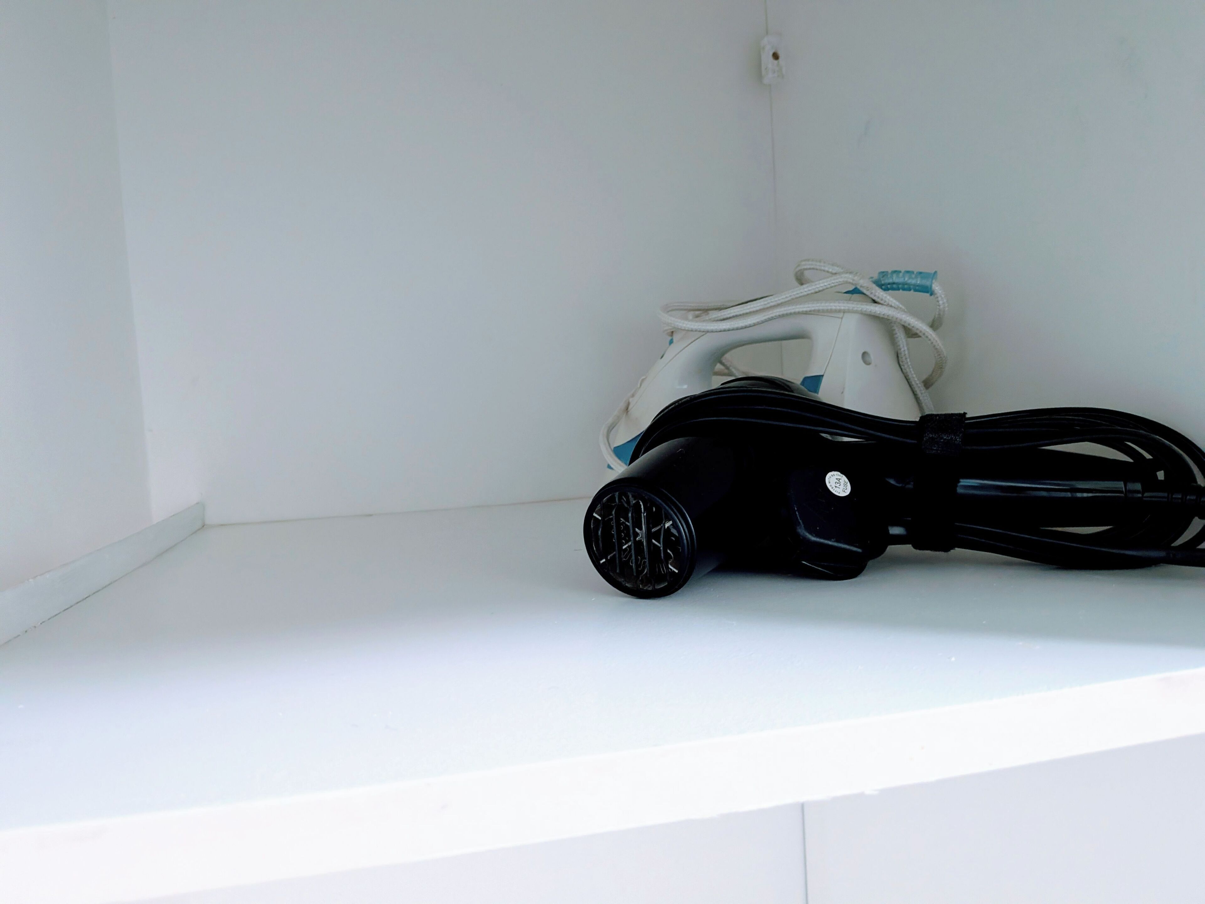 A white shelf with a black and white appliance, possibly a vacuum cleaner, and a white corded device.