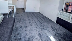 Une pièce de taille modeste, avec un tapis gris, un bureau blanc, une chaise blanche, un canapé blanc, une armoire blanche, une porte blanche et un luminaire au plafond.