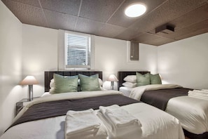 Una habitación de hotel con dos camas, una ventana con persianas, una lámpara de techo y una mesita de noche con lámpara.