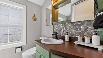 A bathroom with a white toilet, a round sink, a mirror, and a hexagonal tile backsplash.