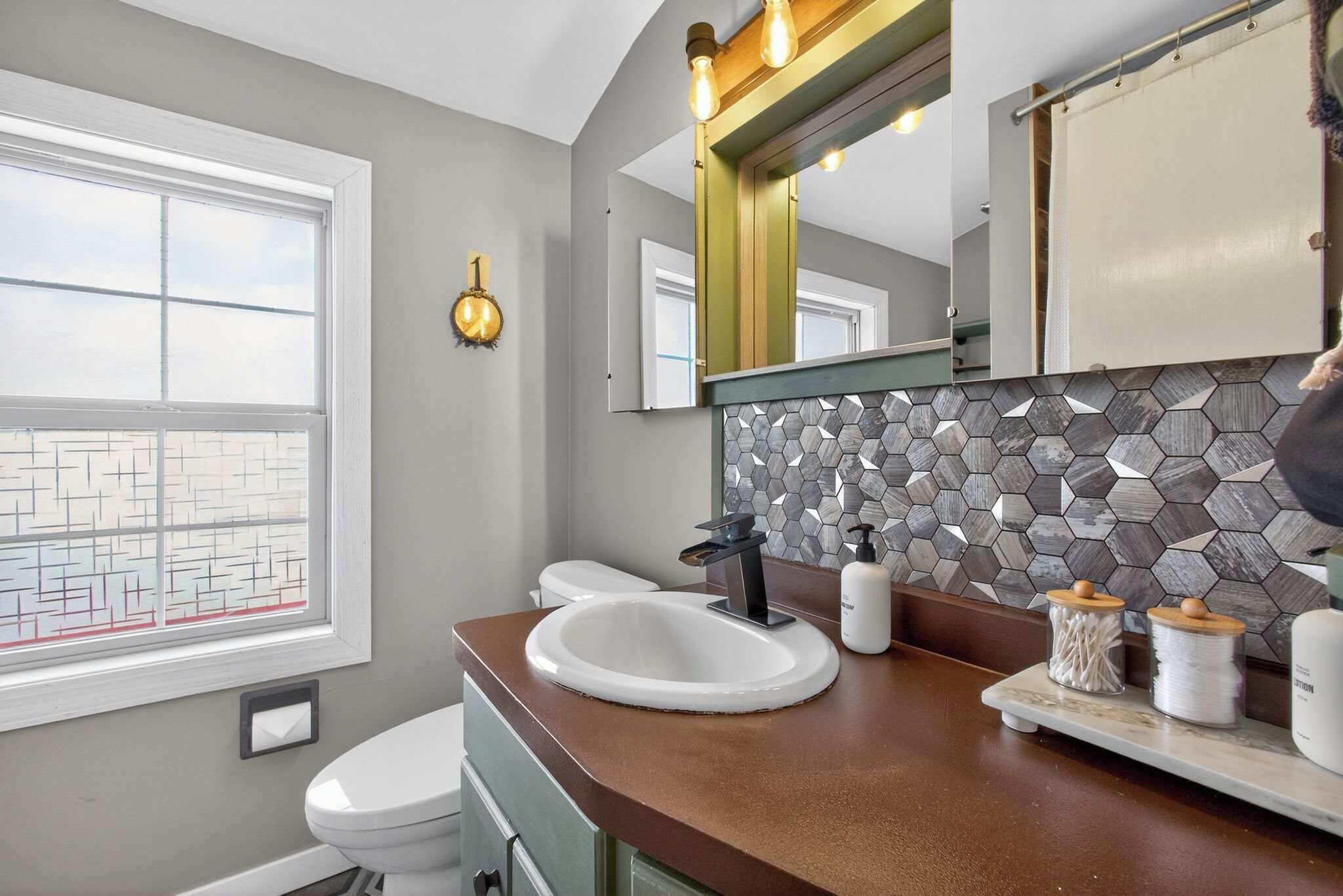A bathroom with a white sink, a toilet, a mirror, and a window.