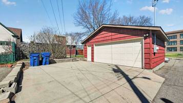 A red garage with a white door, a concrete driveway, and two blue trash bins.