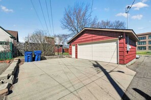 A red garage with a white door, a concrete driveway, and two blue trash bins.