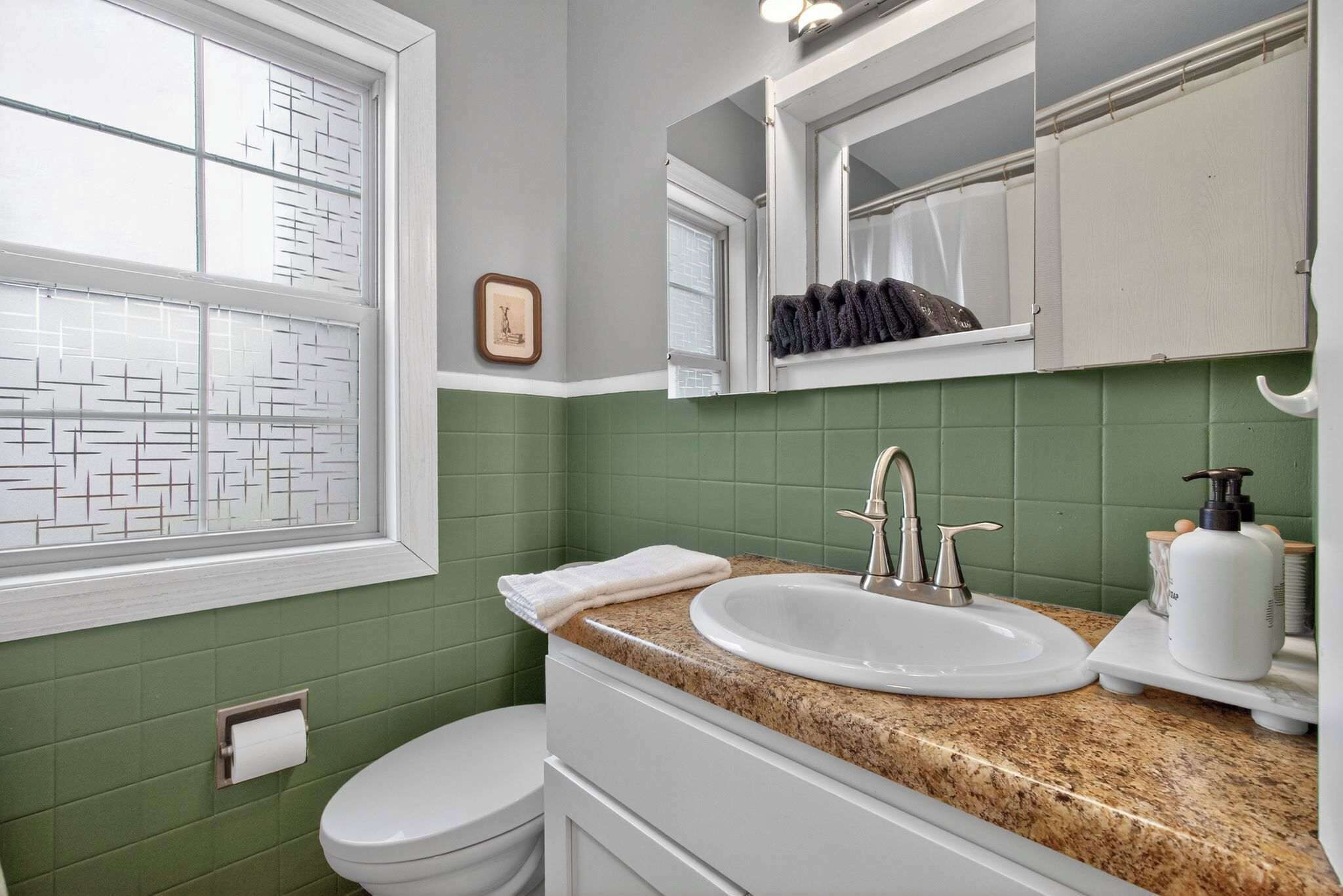 A bathroom with a white toilet, a sink with a faucet, a mirror above the sink, and a window with frosted glass.