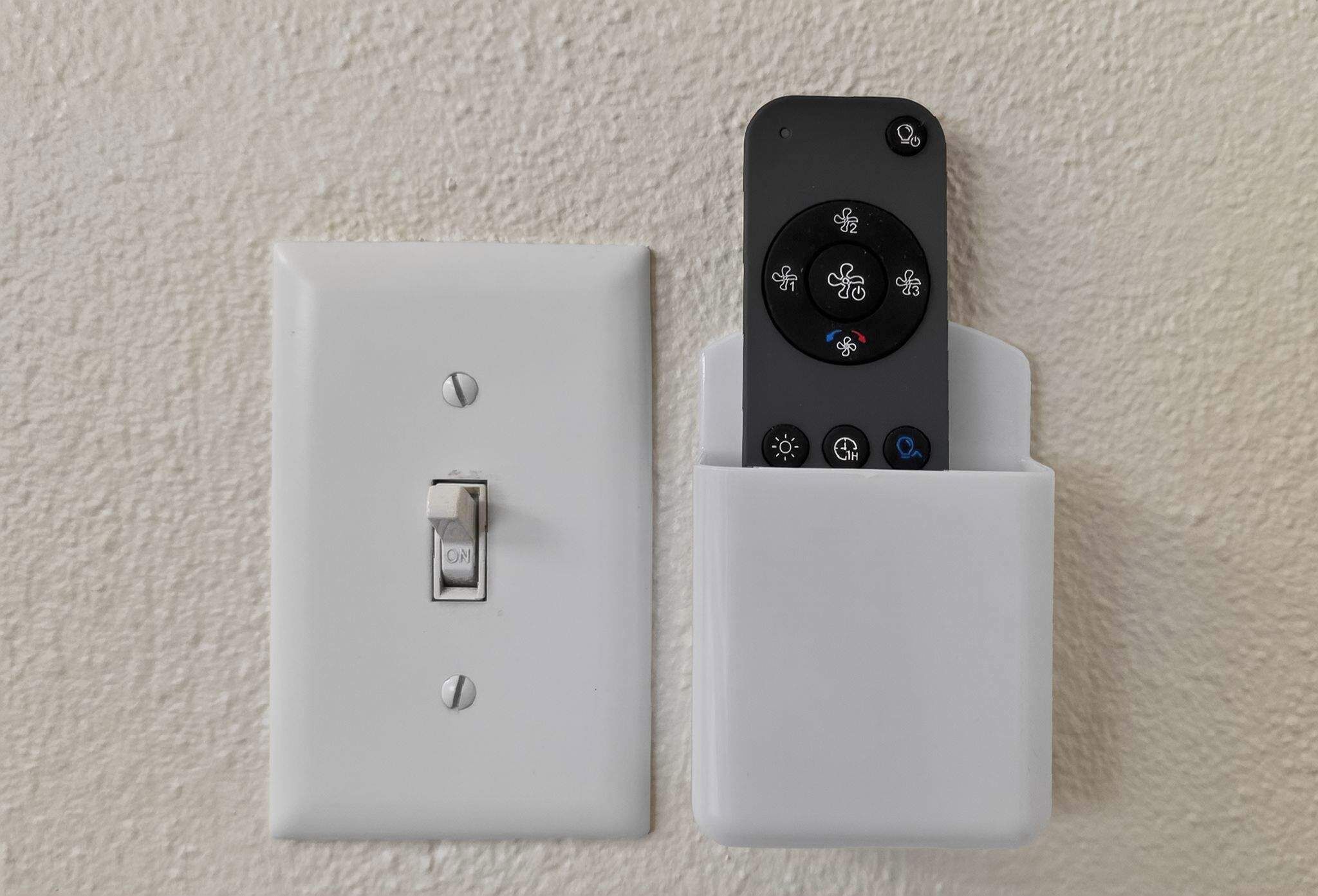 Ein an der Wand befestigter Lichtschalter und eine Fernbedienung in einer weißen Halterung.