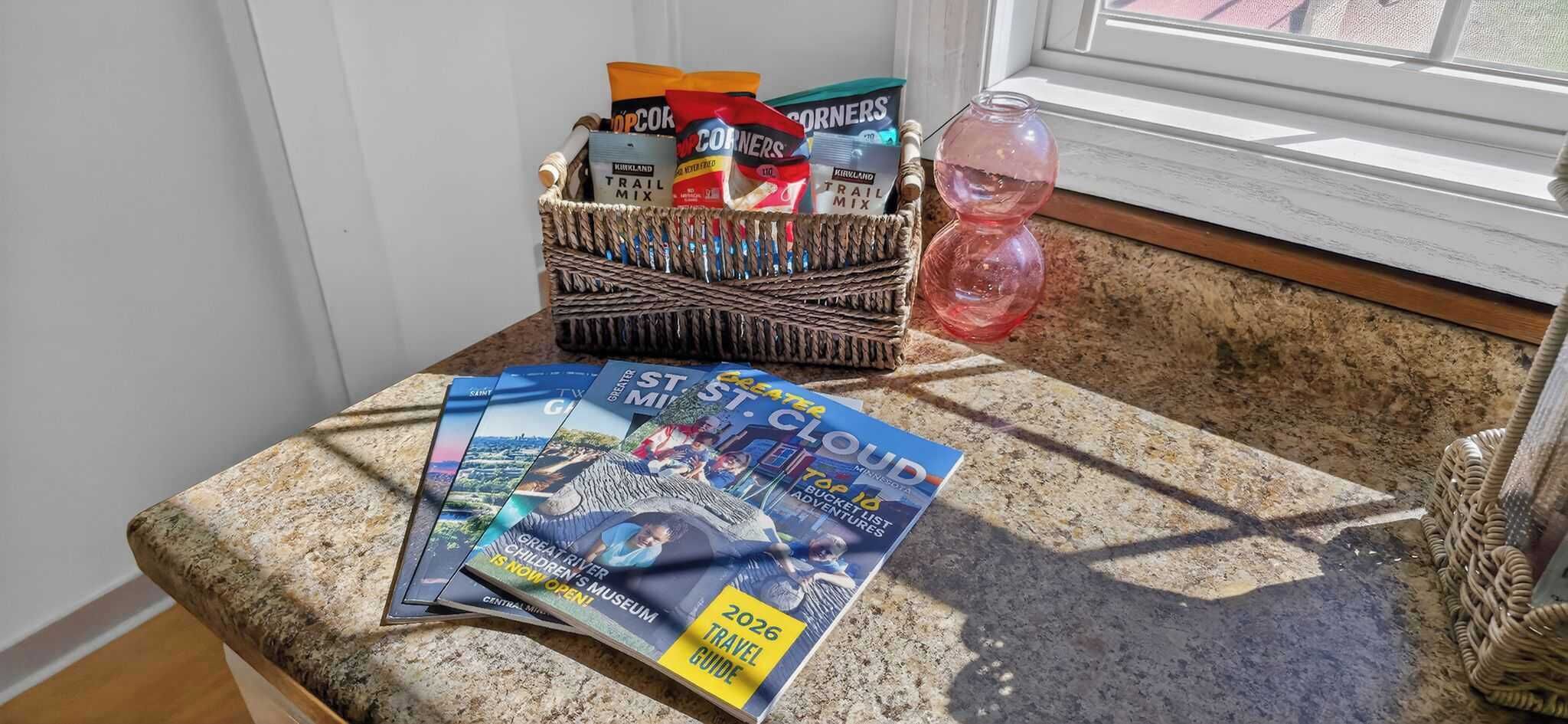 Encimera de granito con una cesta que contiene bolsas de palomitas, una botella de agua y revistas.