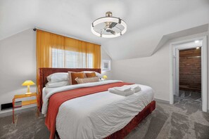 A bedroom with a bed, a bedside table with a lamp, a ceiling fan, and a window with curtains.