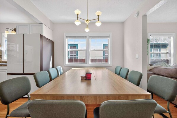 A modern kitchen with white cabinets, a wooden dining table, and a chandelier.