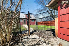 Ein umzÀunter Garten mit einem roten GebÀude, einem Holzpfosten und blauem Himmel.
