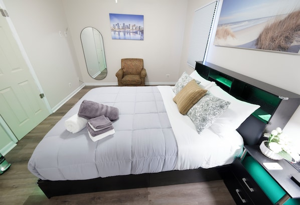 A bedroom with a bed, a chair, a desk, a mirror, and artwork on the walls.