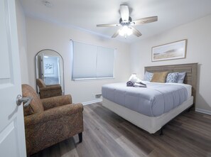 A bedroom with a bed, a chair, a ceiling fan, a window with blinds, and a framed picture on the wall.