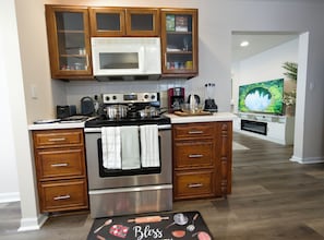 A kitchen with wooden cabinets, a microwave, stove, and a television in the background.