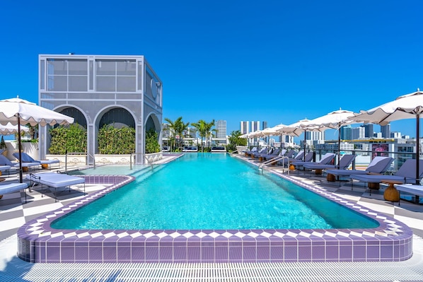 Ein Swimmingpool mit Liegestühlen und Sonnenschirmen, umgeben von einem modernen Gebäude mit Rundbogenfenstern.