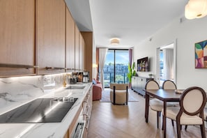 Eine moderne Küche mit einer großen Kochinsel, einem Essbereich mit Holztisch und -stühlen sowie Blick auf die Stadt durch große Fenster.