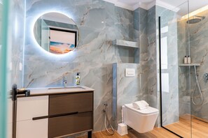 A modern bathroom with a marble wall, a round mirror, a toilet, and a glass-enclosed shower.