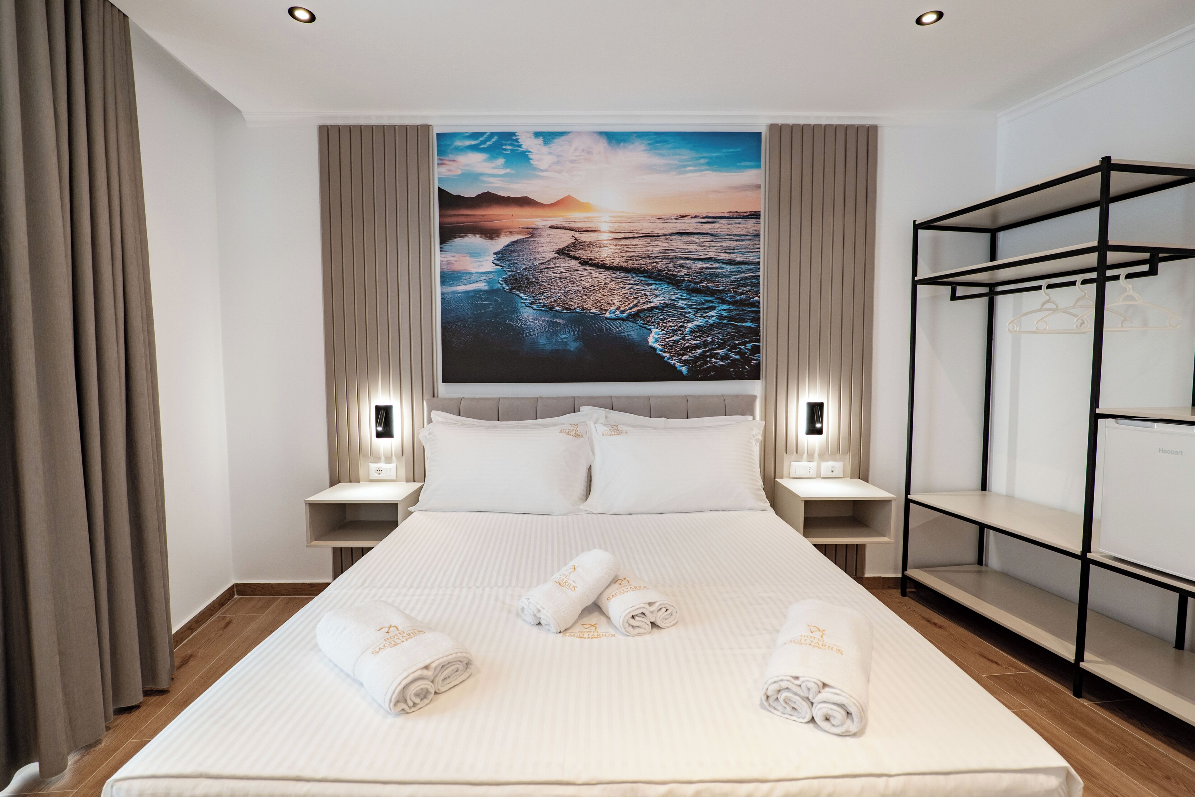 Habitación de hotel con una cama grande, dos mesitas de noche, un armario y un cuadro grande con un paisaje.