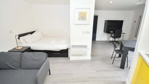 A modern hotel room with a bed, a sofa, a desk with a chair, and a TV. - Bright & Contemporary Studio in Sheffield w WiFi (Sheffield)