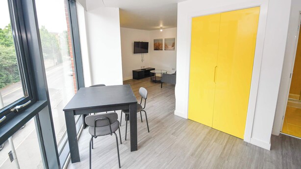 A modern interior with a dining area, a yellow wardrobe, and a TV mounted on the wall. - Bright & Contemporary Studio in Sheffield w WiFi (Sheffield)