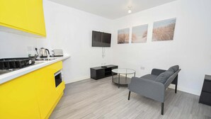 A modern kitchen with yellow cabinets, a flat-screen TV, and a dining area with a gray sofa and a small round table. - Bright & Contemporary Studio in Sheffield w WiFi (Sheffield)