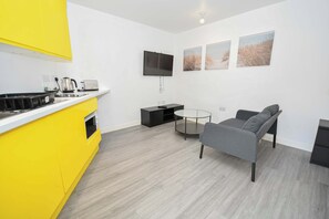 Eine moderne Küche mit gelben Schränken, einem Flachbildfernseher und einem Essbereich mit grauem Sofa und einem kleinen runden Tisch.