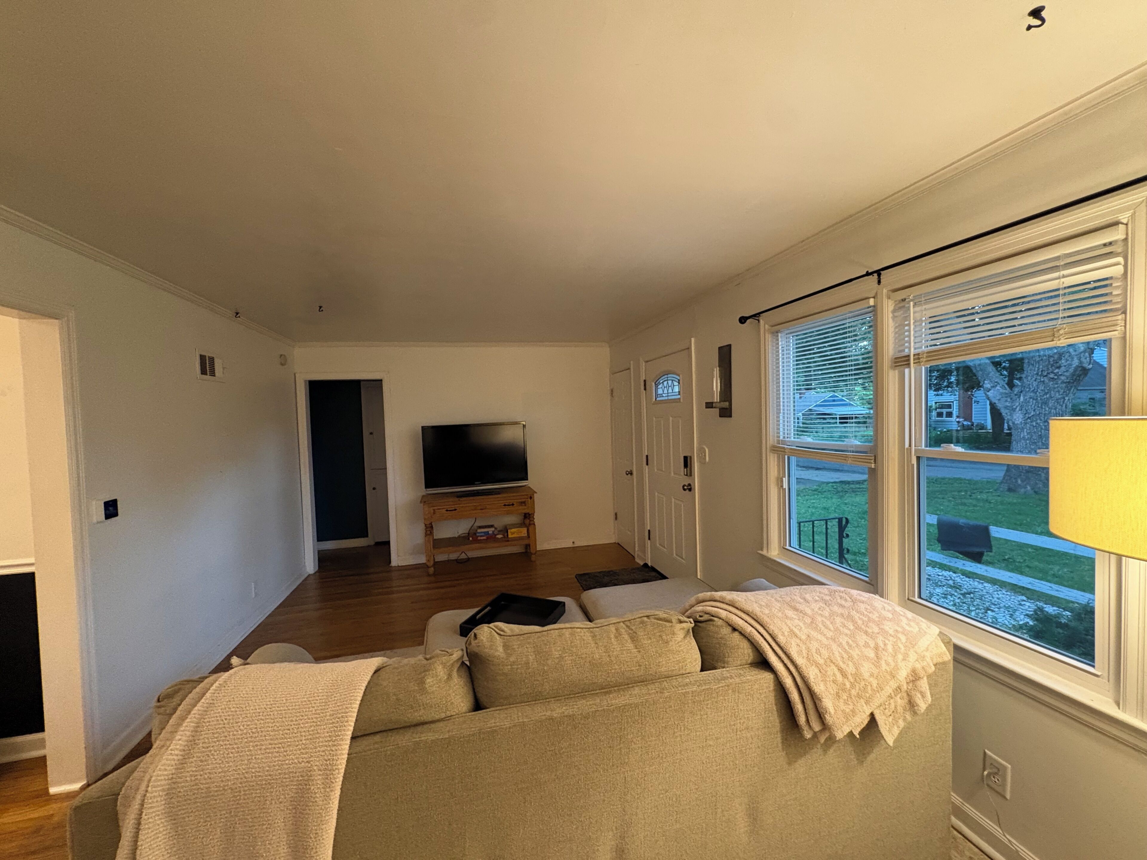 A living room with a sofa, a television on a stand, and a window with blinds.