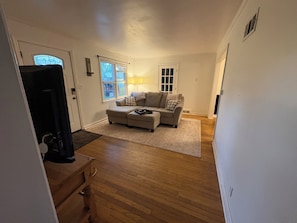 Ein Wohnzimmer mit einem Ecksofa, Holzboden, einer Lampe und einem Fernseher.