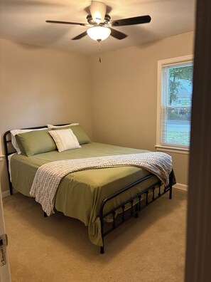 Ein Schlafzimmer mit Bett, Deckenventilator, Fenster mit Jalousien und Teppichboden.
