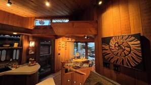 Un intérieur en bois comprenant un coin cuisine, une table à manger et une grande œuvre d’art abstraite accrochée au mur.