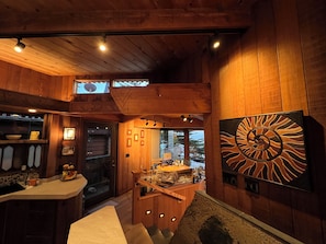 A wooden interior with a kitchen area, a dining table, and a large abstract artwork on the wall.